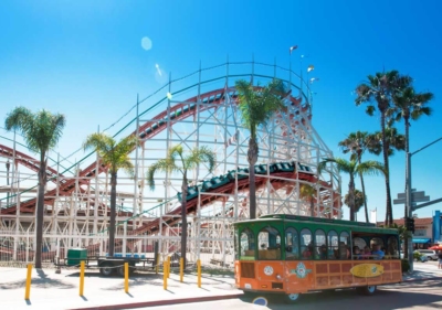 An Old Town Trolley stopped in front of the Belmont Park Rollercoaster with the coaster itself in a high-speed turn