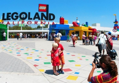 Entrance to Legoland San Diego where 2 young platinum blonde smiling boys are being photographed in front of ticket kiosk made to look as if they were made of Legos
