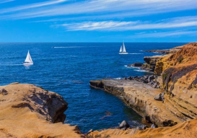 picture of cliffs in the foreground and two sailboats sailing on the ocean in the background