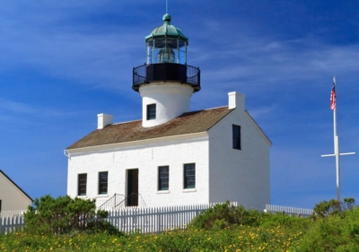 picture of a small white washed house with one door, two windows on each side, a lighthouse jutting out and a picket fence running along the side