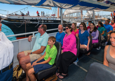 inside of seal tour vehicle showing tour guide speaking to two rows of guests while vehicle is on the water and the star of india tall ship is on the left